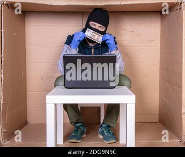thief is holding money in his hands, his face is covered with a balaclava Stock Photo