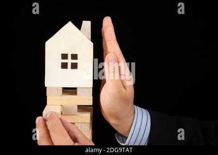 man in suit trying to stop the house falling down from an unstable base concept of policy intervention to the real estate market Stock Photo