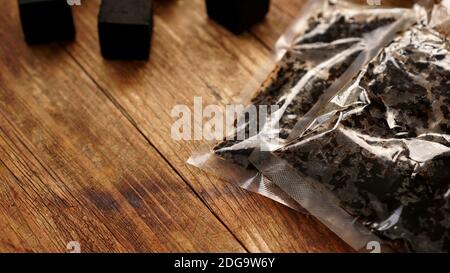 Tobacco in a plastic bag for a hookah on a wooden background with cubes of coconut coal Stock Photo