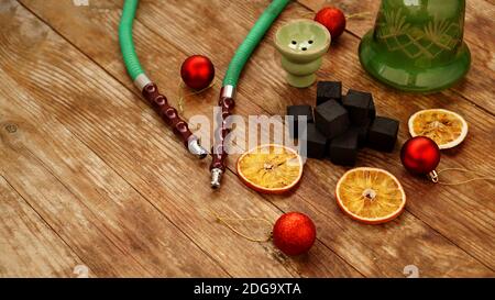 Hookah background for new year and christmas. Hookah, charcoal, dry orange slices and Christmas red balls on a wooden background Stock Photo