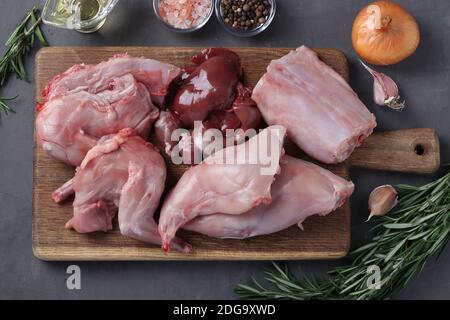 Chopped rabbit carcass on a wooden board and fresh ingredients for cooking. Top view. Closeup Stock Photo