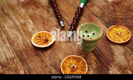 Hookah bowl on wooden background with dry oranges and hookah pipes Stock Photo