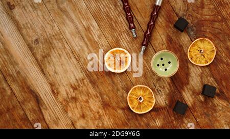 Hookah bowl on wooden background with dry oranges, coal and hookah pipes Stock Photo