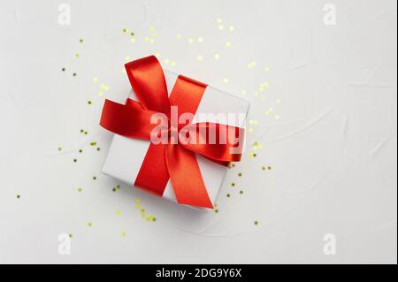 Decorative white gift box with a large red bow on white background with golden little stars. Greeting card template with place for text Stock Photo