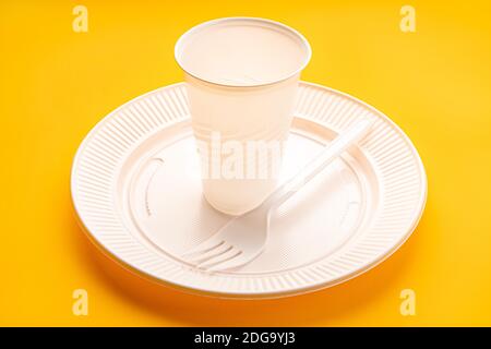 Plastic dishware. White vase, plate and fork on yellow background. Disposable plastic waste Stock Photo