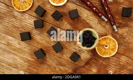 Tobacco in the bowl for hookah on wooden background with coal and dried orange slices Stock Photo