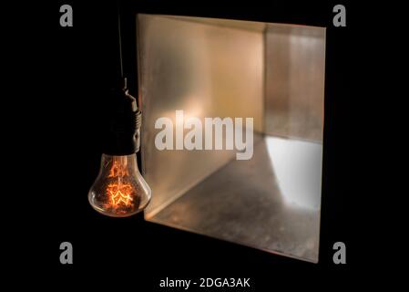 Shine glow lamp bulb without lamp shade in the dark opposite to a square window Stock Photo