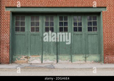 Red brick wall with weathered green garage doors, exterior architectural details, creative copy space, horizontal aspect Stock Photo