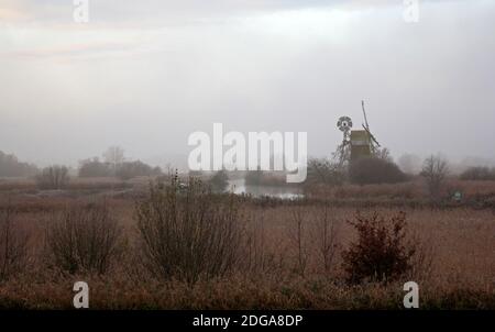 An atmospheric landscape on the Norfolk Broads by the River Ant on a misty December morning with iconic windmill at Ludham, Norfolk, England, UK. Stock Photo