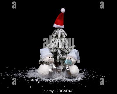 New year and Christmas composition. Snowmen standing in front of Christmas tree with masks. Coronavirus concept background. Stock Photo