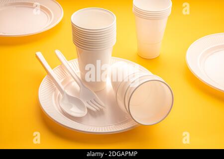 Disposable plastic dishware waste. Group of empty plates, cups, spoons, forks and utensils on yellow table Stock Photo