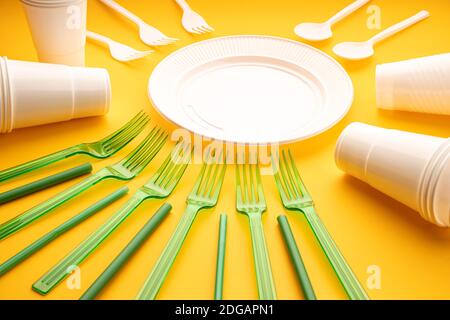 Disposable plastic dishware waste. Group of empty plates, cups, spoons, forks and utensils on yellow table Stock Photo