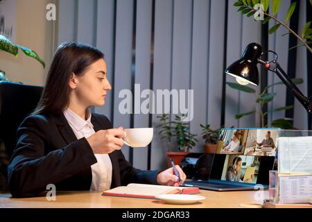 Coffee. Young woman talking, working in videoconference with colleagues, co-workers at home. Online business, education during coronavirus insulation and quarantine. Work, finance, modern tech concept. Stock Photo
