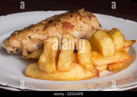 Close-up of French fries on a ceramic plate with chicken and vegetables in the background. Food presentation. Stock Photo
