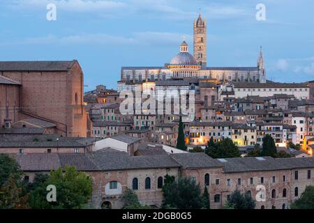 Cityscape view showing the Duomo di Siena illuminated in the evening, as seen from Fortezza Medicea, Siena, Tuscany, Italy Stock Photo