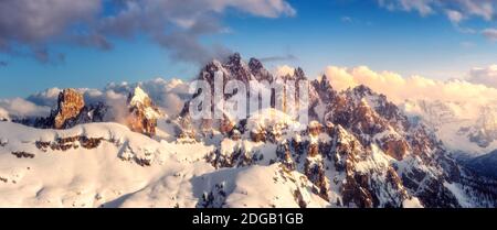 Snowy mountains in low clouds and blue sky at sunset in winter Stock Photo