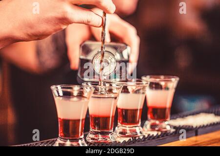 Shots at the nightclub. Red alcoholic drink in glasses on bar. Red cocktail at the nightclub. Barman preparing cocktail shooter Stock Photo