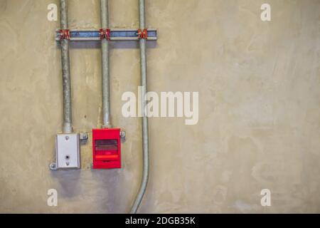 Red fire alarm pull box emergency and fire fighters telephone with conduit pipeline on concrete wall. Stock Photo