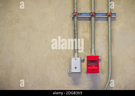 Red fire alarm pull box emergency and fire fighters telephone with conduit pipeline on concrete wall. Stock Photo