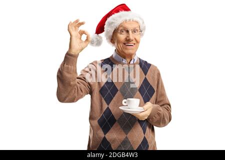 Elderly man with a cup of coffee making a perfect sign and wearing a santa claus hat isolated on white background Stock Photo