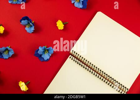 Flat design photo on red background with place for text, decorative flowers, blank notepad, top view, beautiful composition Stock Photo