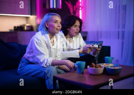 Handsome young man teaching how to play the video games to his girlfriend, on the couch, concept about home entertainment, video games. Stock Photo