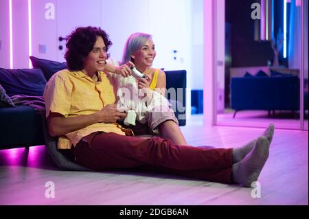 Couple at home playing video games. Girl hug the boy and holding joystick in her hands. Spendning time together at home. Stock Photo