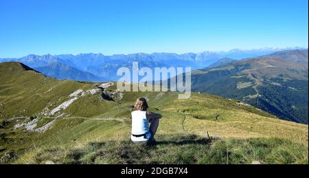 Caucasian woman looking from Mount Guglielmo near Lake Iseo to other summits and the Alps. Brescia, Lombardy, Italy. Stock Photo