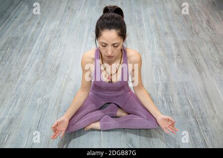 Portrait of adult woman practicing yoga in meditation posture. She is sitting on a wooden floor. Space for text. Stock Photo