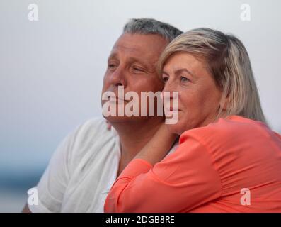 A middle aged couple sitting close to each other and looking into the distance, smiling Stock Photo