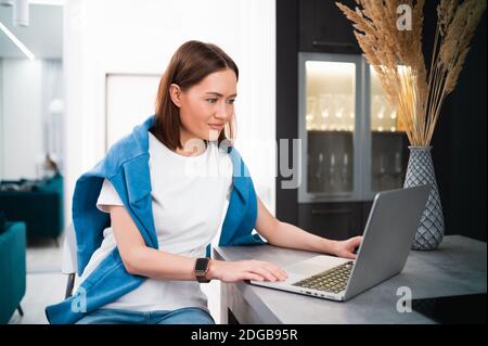 Woman on remote work or online education, using laptop computer, making notes, indoors at home. Online business, young professional at workplace Stock Photo