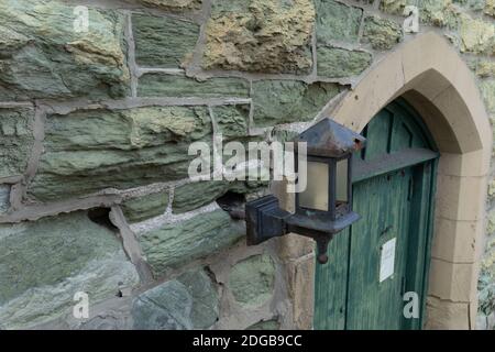 Crumbling green limestone wall, old metal lamp and green weathered door, church exterior, horizontal aspect Stock Photo