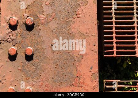 Industrial background with peeling paint on rusted metal flanked by large bolts and metal grate, creative copy space, horizontal aspect Stock Photo