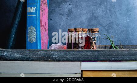 Shelf made out off books and a wooden tray, containing a diary, rock salt, glass stopper bottles with spices an air plant and a notebook. Gray texture Stock Photo