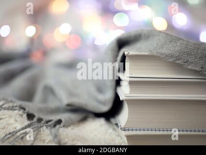 A woolen warm knitted blanket, colorful lights for home decor and a pile of books on the bed. Time to read at home. Cozy and comfortable atmosphere Stock Photo