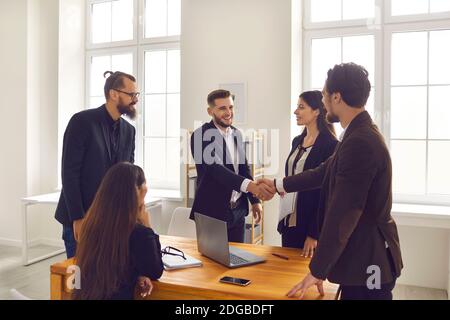 Young business people closing deal and shaking hands after successful negotiation in company office Stock Photo