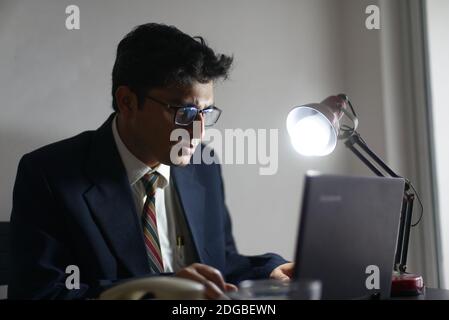 An Indian Bengali tall, dark, handsome brunette young man/telecaller in office wear is sitting on a office table in working mood in corporate office Stock Photo