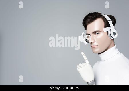 Cyborg man in headphones with artificial hand pointing with finger isolated on grey Stock Photo
