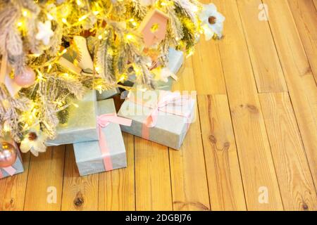 From above wrapped gift boxes placed on wooden floor near Christmas tree decorated with fairy lights Stock Photo