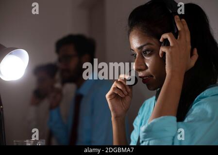 An Indian Bengali brunette young woman/telecaller in office wear is sitting on a office table in a working mood in a corporate office/bpo/call center. Stock Photo
