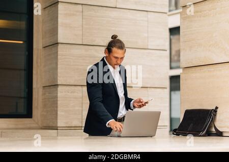 Businessman working over laptop near office building Stock Photo
