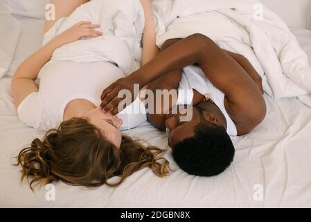 Mixed race couple lying in bed looking at each other Stock Photo