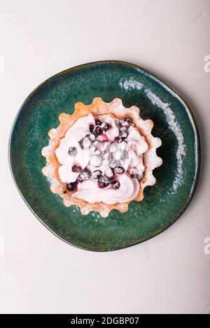 Vertical photo of delicious small tartlets with berries and whipped cream in a green plate over white background. Stock Photo