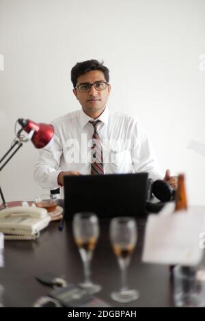 Indian Bengali tall, dark, handsome brunette young man in office wear enjoying success while sitting on an office table  in a corporate office/bpo Stock Photo