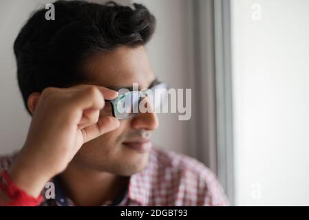 Portrait of an Indian Bengali tall, dark, handsome brunette young man in office wear is standing in front of a glass window in a corporate office/bpo Stock Photo