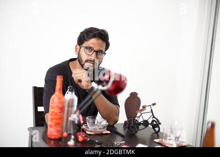 An Indian Bengali tall, dark, handsome beard brunette young man in casual t-shirt is sitting on a office table in a creative mood. Stock Photo