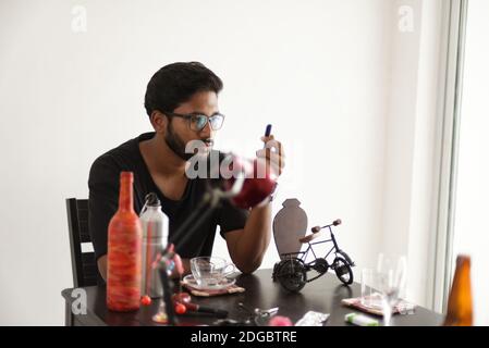 An Indian Bengali tall, dark, handsome beard brunette young man in casual t-shirt is sitting on a office table in a creative mood. Stock Photo