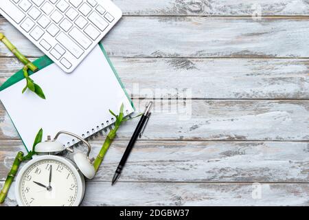 tHome office workspace with computer keyboard, blank paper clipboard, alarm clock and green bamboo plant on wooden background. Flat lay, top view. Wor Stock Photo