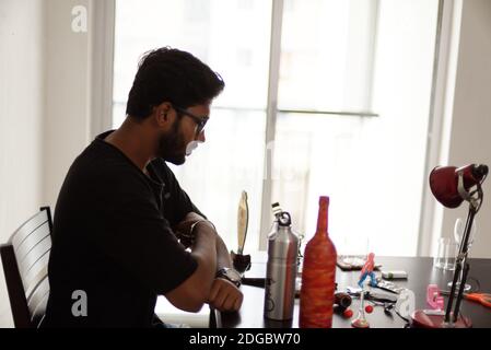 An Indian Bengali tall, dark, handsome beard brunette young man in casual t-shirt is sitting on a office table in a creative mood. Stock Photo