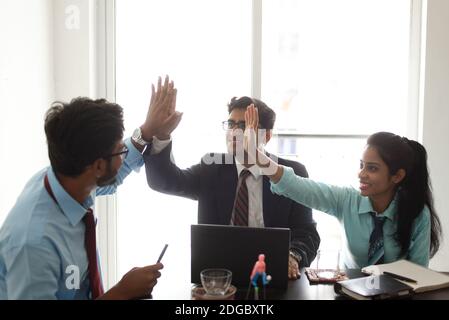 Young and energetic Indian Bengali corporate employees are celebrating success and teamwork through hand gestures. Indian corporate Stock Photo
